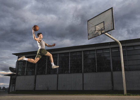 Young man jumping while playing basketball - STSF02925