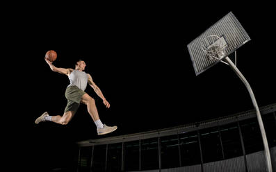 Junger Mann springt beim Basketballspielen in der Nacht - STSF02930