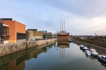 Germany, Bavaria, Wurzburg, Power station reflecting on shiny surface of city canal - NDF01270