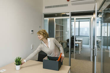 Mature businesswoman arranging desk in office - XLGF01473