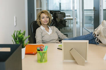 Female professional with feet up looking away while sitting at desk in office - XLGF01478