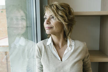 Female entrepreneur with blond hair looking away by window in office - XLGF01480