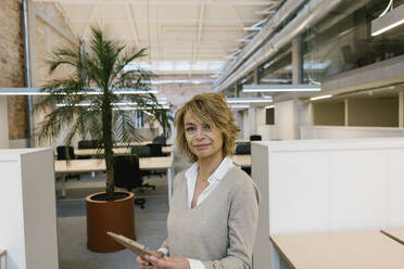 Mature businesswoman holding digital tablet in coworking office - XLGF01486