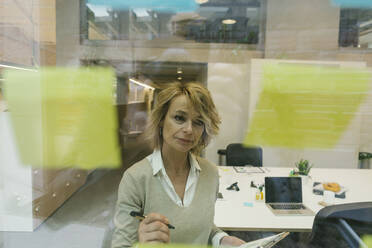 Matre businesswoman looking at adhesive notes while working in coworking office - XLGF01488