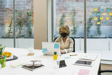 Businesswoman wearing protective face mask working on laptop at desk - XLGF01490