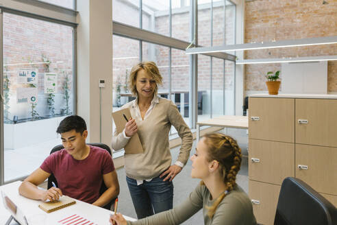 Lächelnde weibliche Fachkräfte, die mit einem männlichen Kollegen in einem Coworking-Büro diskutieren - XLGF01506