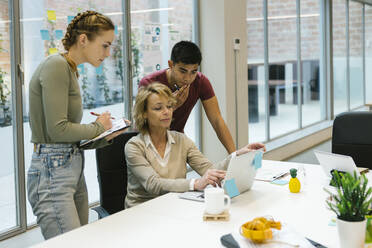Geschäftsfrau diskutiert über Laptop mit männlichen und weiblichen Kollegen am Schreibtisch - XLGF01512