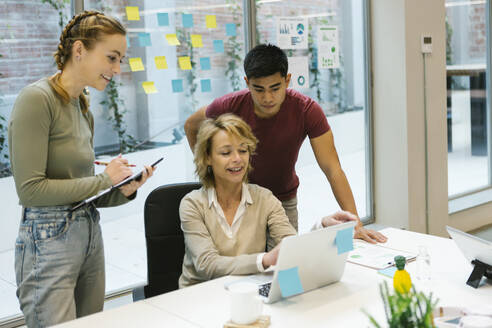 Female professional explaining business plan on laptop to coworkers in office - XLGF01513