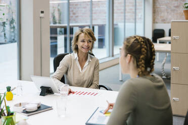 Smiling businesswoman discussing with female coworker at desk - XLGF01514