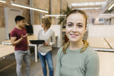 Geschäftsfrau lächelnd mit Kollegen diskutieren im Hintergrund im Büro - XLGF01532