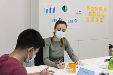 Male and female professional wearing protective face mask working at desk in coworking office during pandemic - XLGF01543