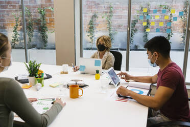 Mature businesswoman wearing protective face mask discussing with coworkers during COVID-19 - XLGF01545