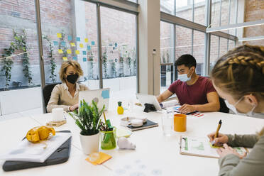 Male and female professionals working at hot desk during COVID-19 - XLGF01546