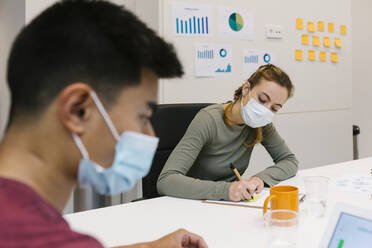 Male and female professional wearing protective face mask working at hot desk in coworking office - XLGF01548