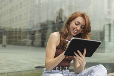 Beautiful young woman using digital tablet in front of glass wall - MTBF00957