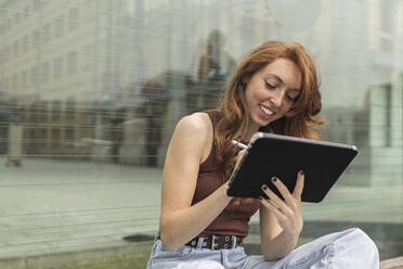 Schöne junge Frau mit digitalem Tablet vor einer Glaswand - MTBF00957