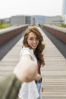 Freundin lächelt, während sie die Hand ihres Freundes auf einer Brücke hält - MTBF00971