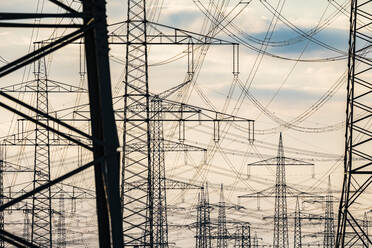 Germany, North Rhine Westphalia, Niederaussem, Electricity pylons against cloudy sky at sunset - JATF01310