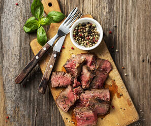 Basil, forks, peppercorns and steak lying on cutting board - KSWF02191