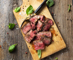 Basil, fork, peppercorns and steak lying on cutting board - KSWF02192