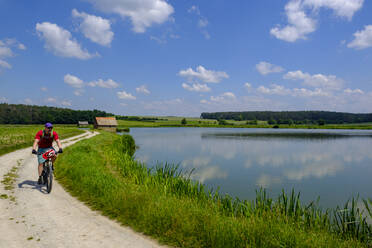 Germany, Franconia, Uehlfeld, Mature man cycling along carp pond - LBF03519