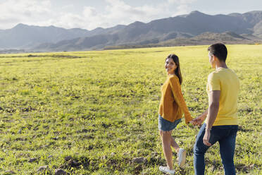 Girlfriend holding hand of boyfriend while walking on meadow - MIMFF00680