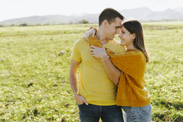 Happy girlfriend embracing boyfriend standing in grass - MIMFF00682