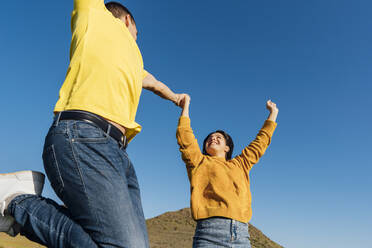 Glückliches junges Paar springt mit erhobenen Armen an einem sonnigen Tag - MIMFF00690