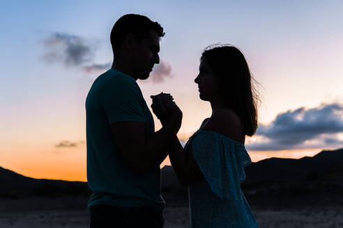 Couple holding hands while standing outdoors during sunset - MIMFF00710