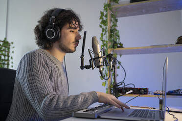 Male music composer with sound recording equipment using laptop at home - FBAF01819
