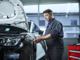 Maintenance engineer installing vehicle part at auto repair shop - CVF01722