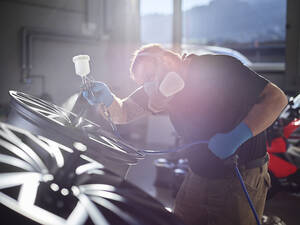Experte lackiert Fahrzeugteil mit Airbrush in der Werkstatt - CVF01728
