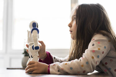 Thoughtful girl looking away while holding robot toy at home - JOSEF04124