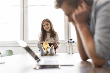 Businessman in front of laptop with smiling girl sitting on table at home - JOSEF04129