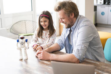 Smiling father and daughter looking at robot toy on table - JOSEF04155