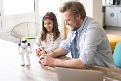 Lächelnder Vater und Tochter betrachten ein Roboterspielzeug auf dem Tisch - JOSEF04155