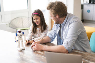 Mature man looking at smiling daughter playing with robot toy at home - JOSEF04156