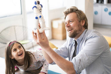 Happy man and girl playing with robot toy at home - JOSEF04157