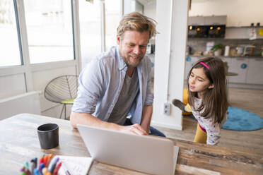 Smiling father teaching daughter through laptop at home - JOSEF04162