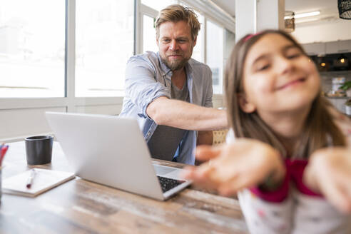 Geschäftsmann schaut auf einen Laptop, während er neben seiner spielenden Tochter zu Hause sitzt - JOSEF04163