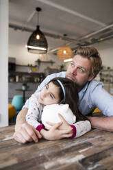 Thoughtful father and daughter with piggy bank looking away at home - JOSEF04164