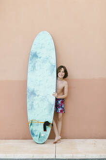 Boy standing with surfboard in front of wall - AGGF00089