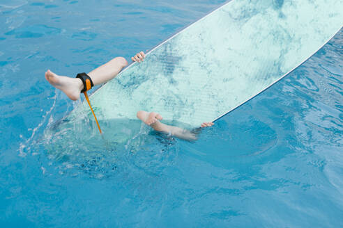 Boy playing with surfboard in swimming pool - AGGF00108