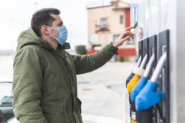 Mann mit Gesichtsschutzmaske an einer Tankstelle während COVID-19 - JAQF00498
