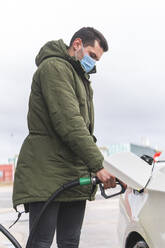 Mann mit Schutzmaske beim Tanken an einer Tankstelle während COVID-19 - JAQF00501