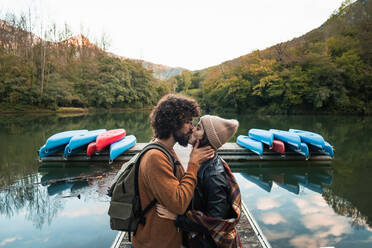 Seitenansicht junges liebendes Paar in warmer Kleidung küssen zärtlich, während stehend auf See hölzernen Kai gegen üppige reichlich bewaldeten Hügeln in Reservoir Valdemurio - ADSF22953