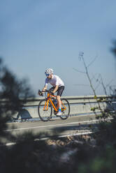 Ganzer Körper eines jungen Sportlers in Sportkleidung und Helm beim Fahrradfahren auf einer asphaltierten Straße an einem sonnigen Tag - ADSF22960