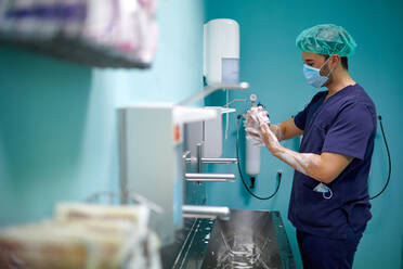 Seitenansicht eines anonymen jungen männlichen Arztes in medizinischer Uniform und Maske, der sich vor einer Operation im Operationssaal die Hände mit Seife wäscht - ADSF22964