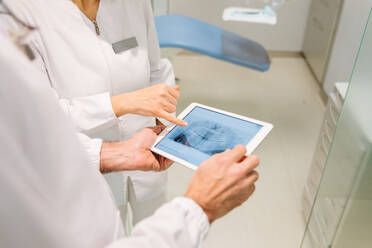 Von oben Ernte anonyme Zahnärzte in medizinischen Roben Prüfung der Zähne Zustand auf Röntgen-Scan auf Tablet während der Arbeit zusammen in der modernen Zahnklinik - ADSF22984
