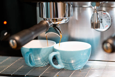 Professional coffee machine pouring coffee into small ceramic cups in coffeehouse with contemporary equipment - ADSF23008